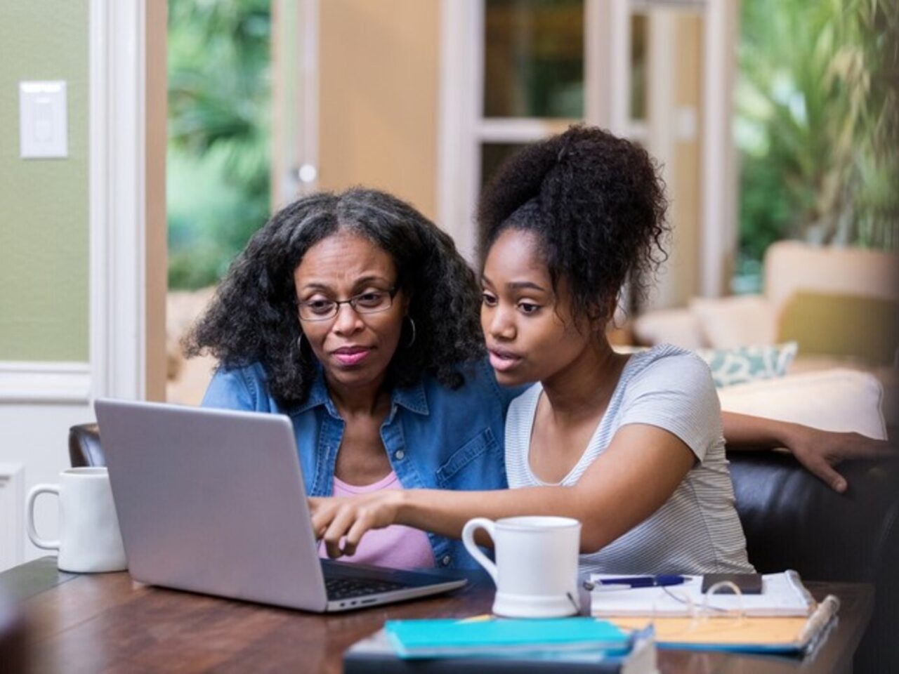 Young woman and her mature mom look at something on a laptop as the young woman studies for a college exam.