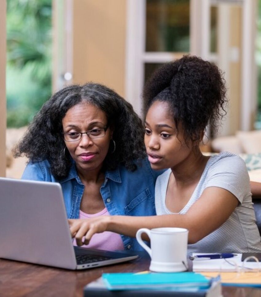 Young woman and her mature mom look at something on a laptop as the young woman studies for a college exam.